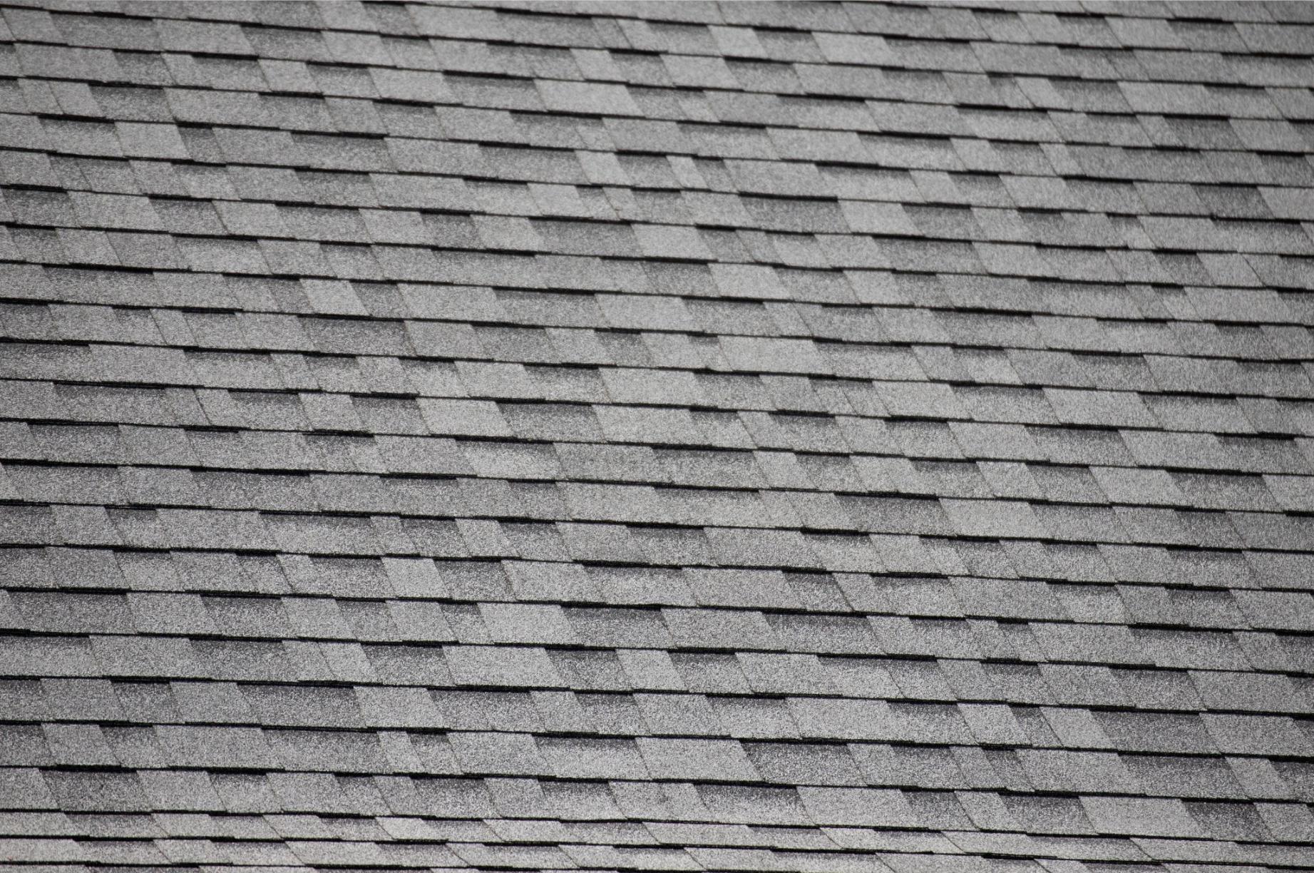 Takshingel av grå asfalt som ligger i ett jämnt, överlappande mönster. Shingelplattorna har en något skrovlig textur och ligger jämnt fördelade över hela den synliga takytan.